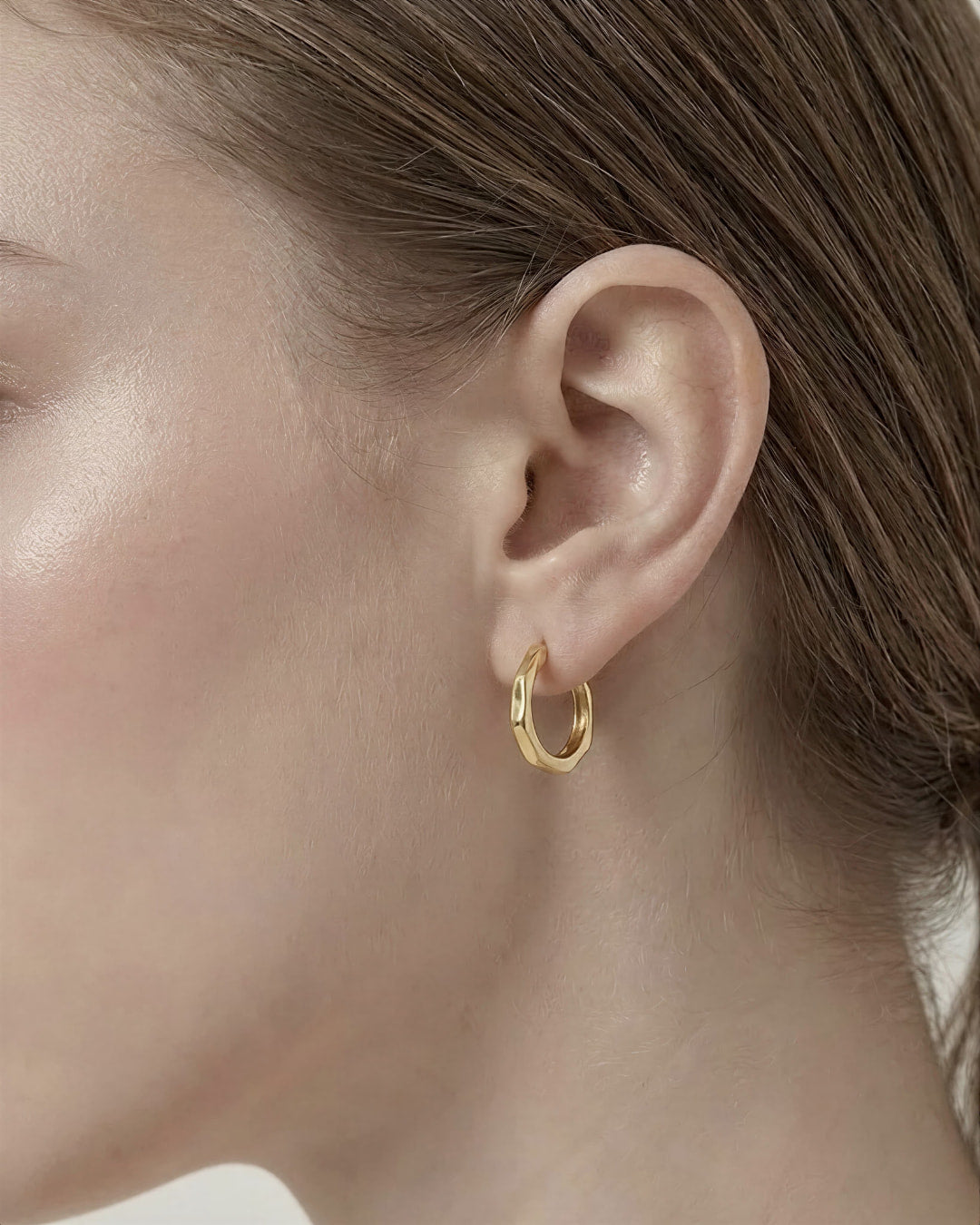 Model wearing Contour Twist Hoop Earrings in 18K gold plated finish featuring a smooth twisted hoop silhouette.