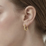 Model wearing Contour Twist Hoop Earrings in 18K gold plated finish featuring a smooth twisted hoop silhouette.