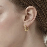 Model wearing Contour Twist Hoop Earrings in 18K gold plated finish featuring a smooth twisted hoop silhouette.