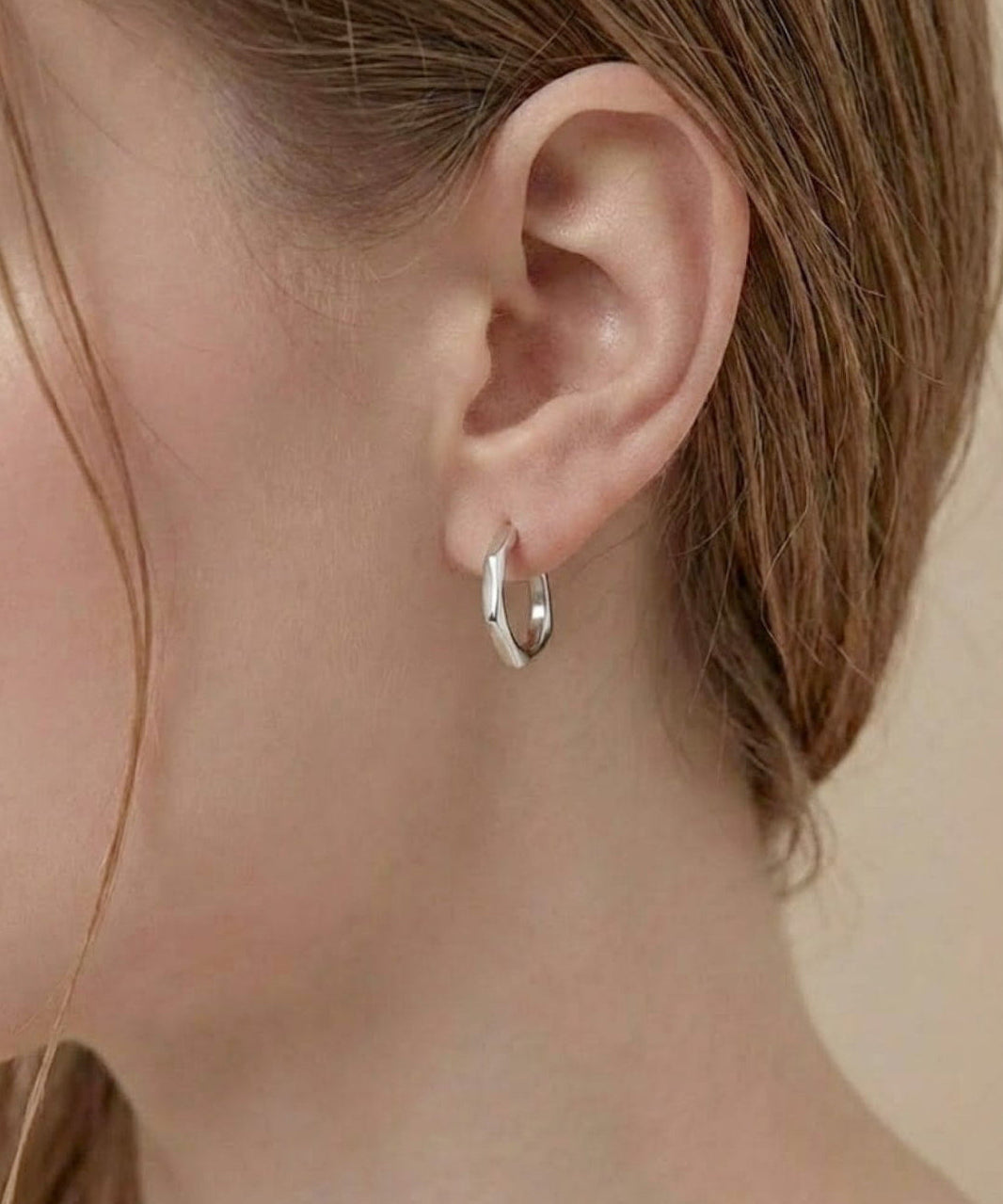 Model wearing Contour Twist Hoop Earrings in platinum plated finish with a softly contoured polished design.
