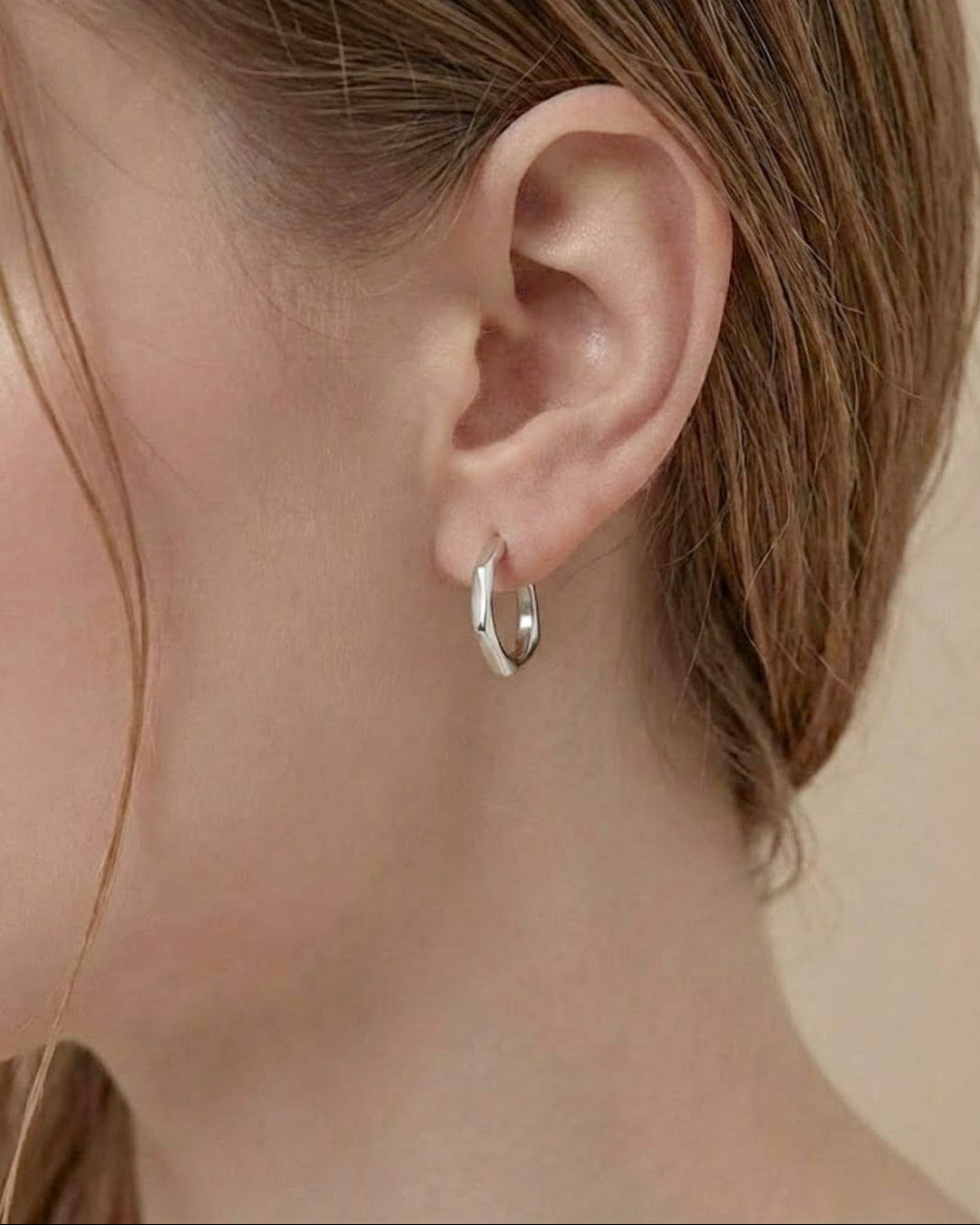 Model wearing Contour Twist Hoop Earrings in platinum plated finish with a softly contoured polished design.

