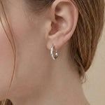 Model wearing Contour Twist Hoop Earrings in platinum plated finish with a softly contoured polished design.

