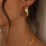 Ease Classic Oval Hoop Earrings in 14k gold plated finish worn on ear with smooth rounded oval silhouette.
