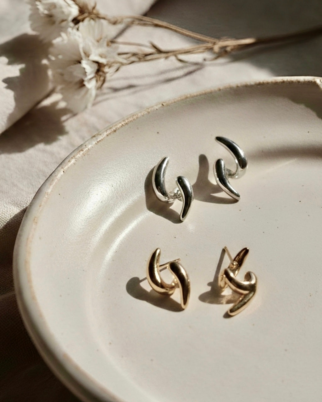 Ease Sculpted Curve Earrings in 18K gold and 925 silver plated finish displayed on a ceramic plate with soft natural lighting.