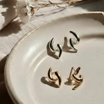 Ease Sculpted Curve Earrings in 18K gold and 925 silver plated finish displayed on a ceramic plate with soft natural lighting.