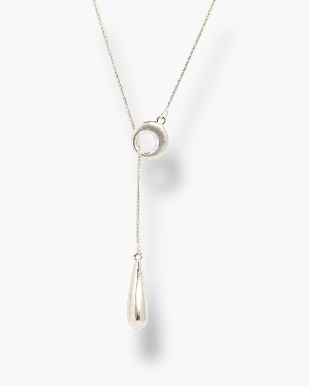 Minimal silver linear drop necklace with circular pendant and long teardrop charm.
