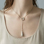 Woman wearing modern silver linear drop pendant necklace with circle detail and vertical drop charm.