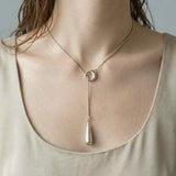 Woman wearing modern silver linear drop pendant necklace with circle detail and vertical drop charm.
