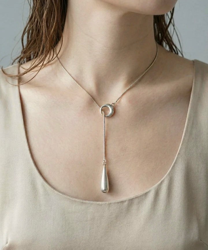 Woman wearing modern silver linear drop pendant necklace with circle detail and vertical drop charm.