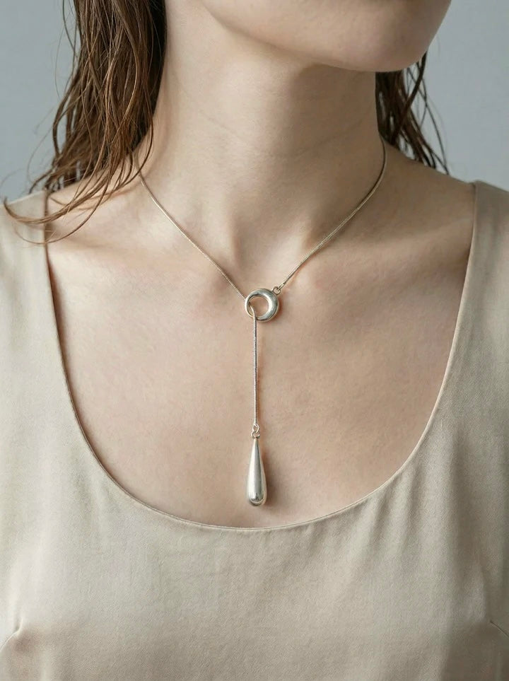 Woman wearing modern silver linear drop pendant necklace with circle detail and vertical drop charm.