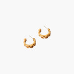 Gold wave cut hoop earrings pair on white background, sculptural minimalist jewelry